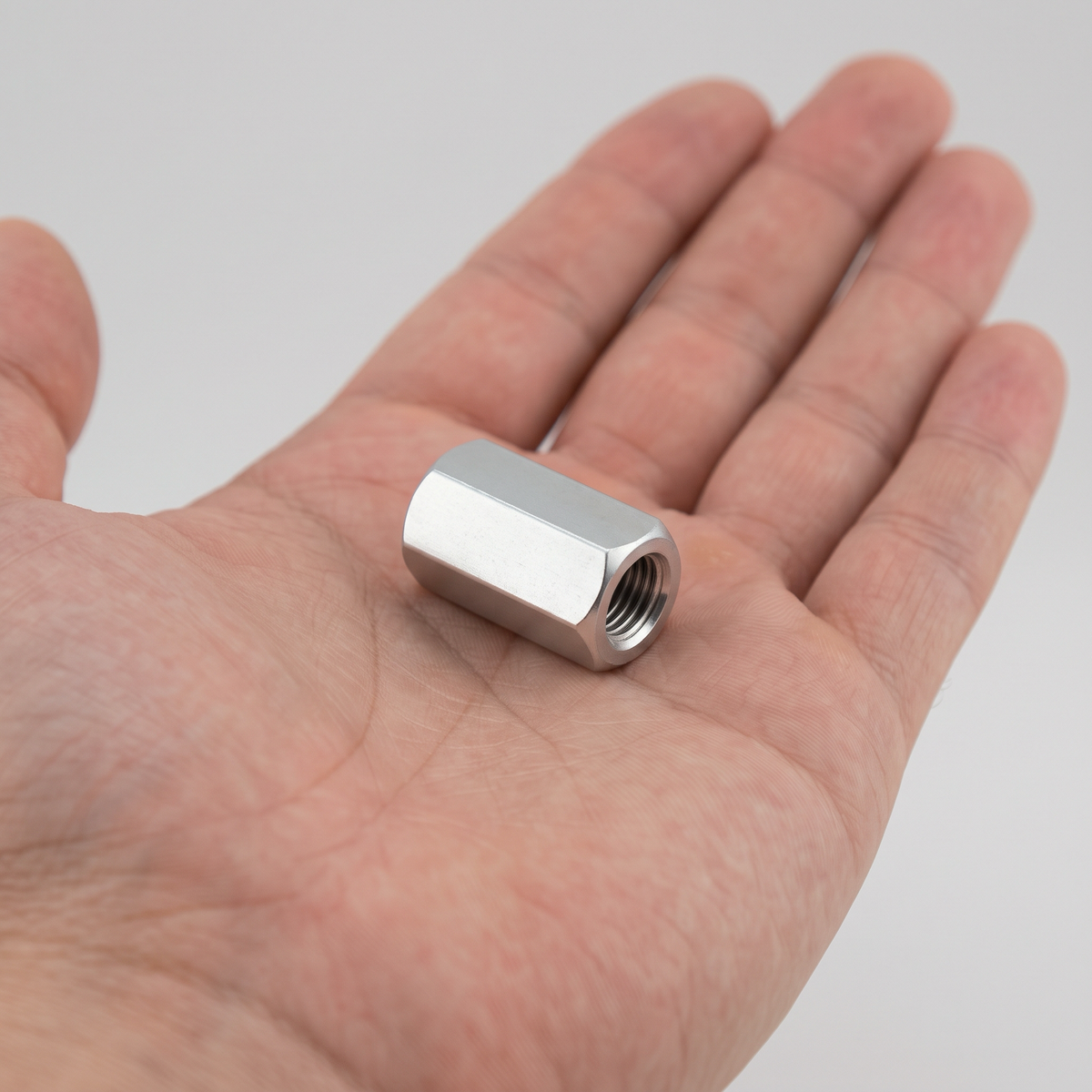 Bright zinc plated hex coupling nut shown in an open hand for scale