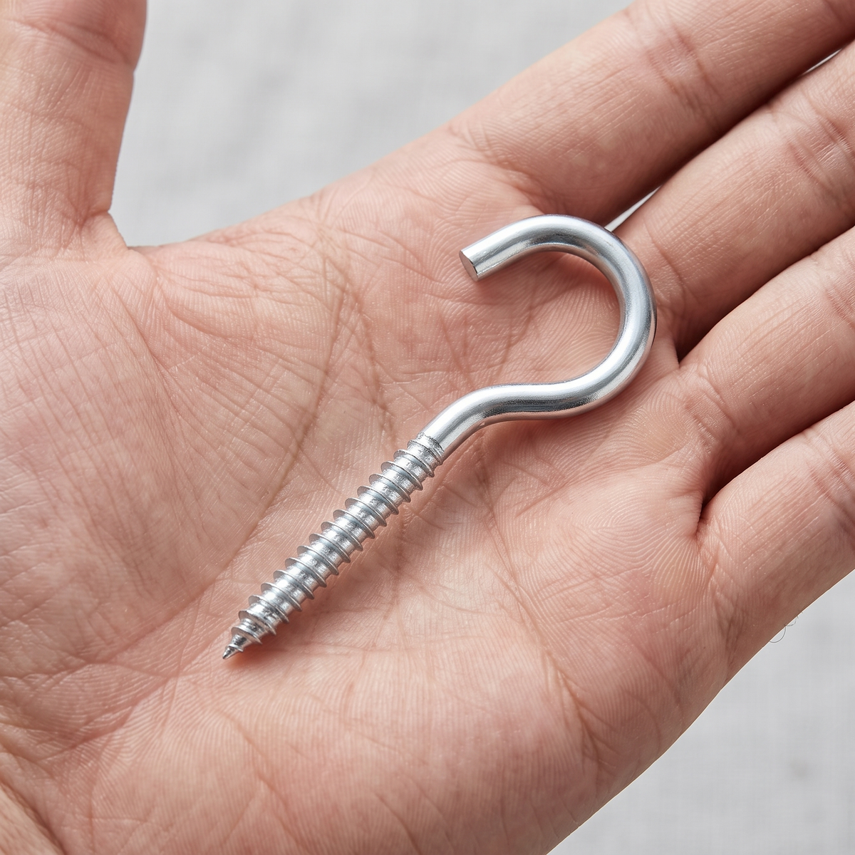 A bright zinc-plated screw-in cup hook shown in an open hand for scale