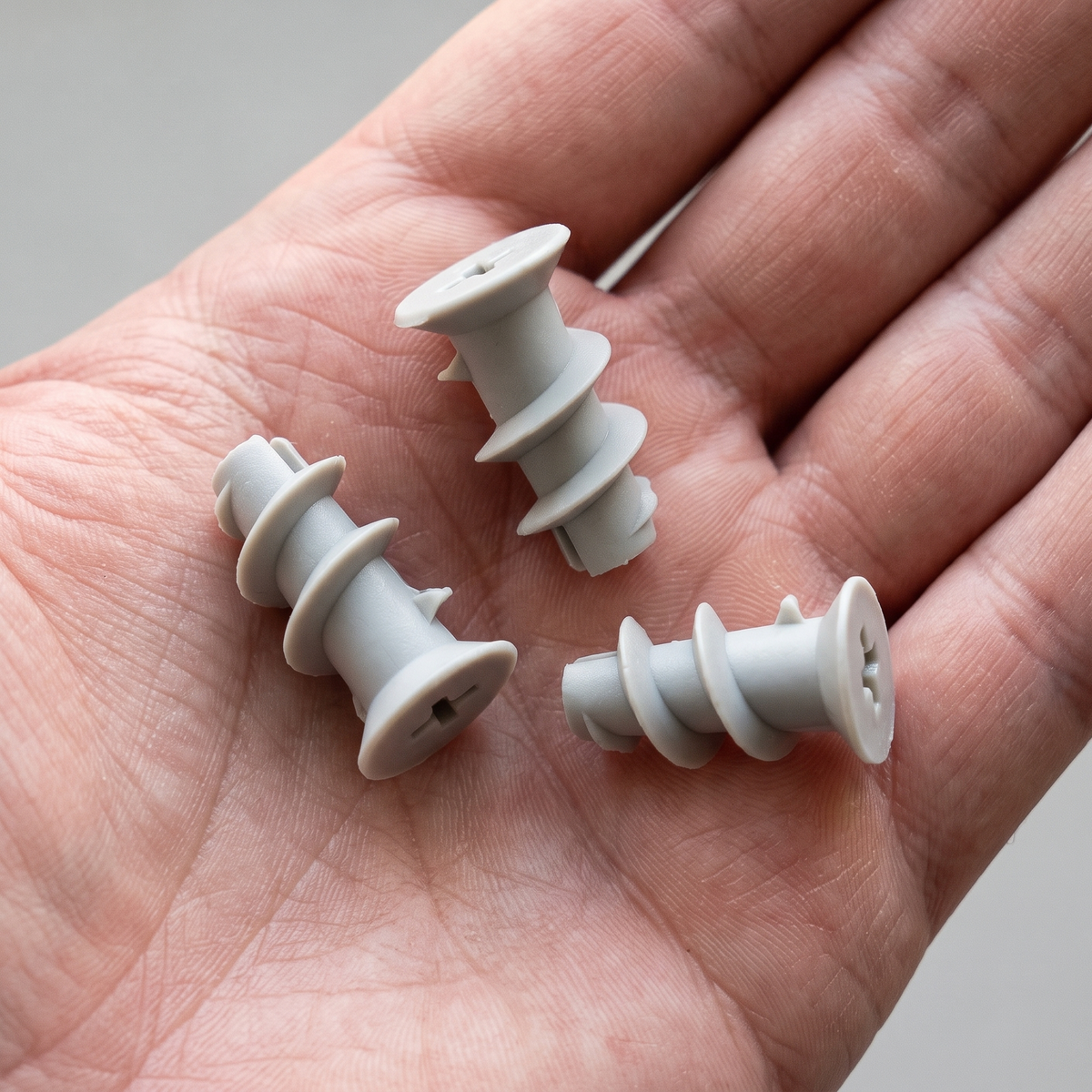 Three grey ABS plastic plasterboard wall plugs, 6 x 24.5mm, shown in an open hand for scale